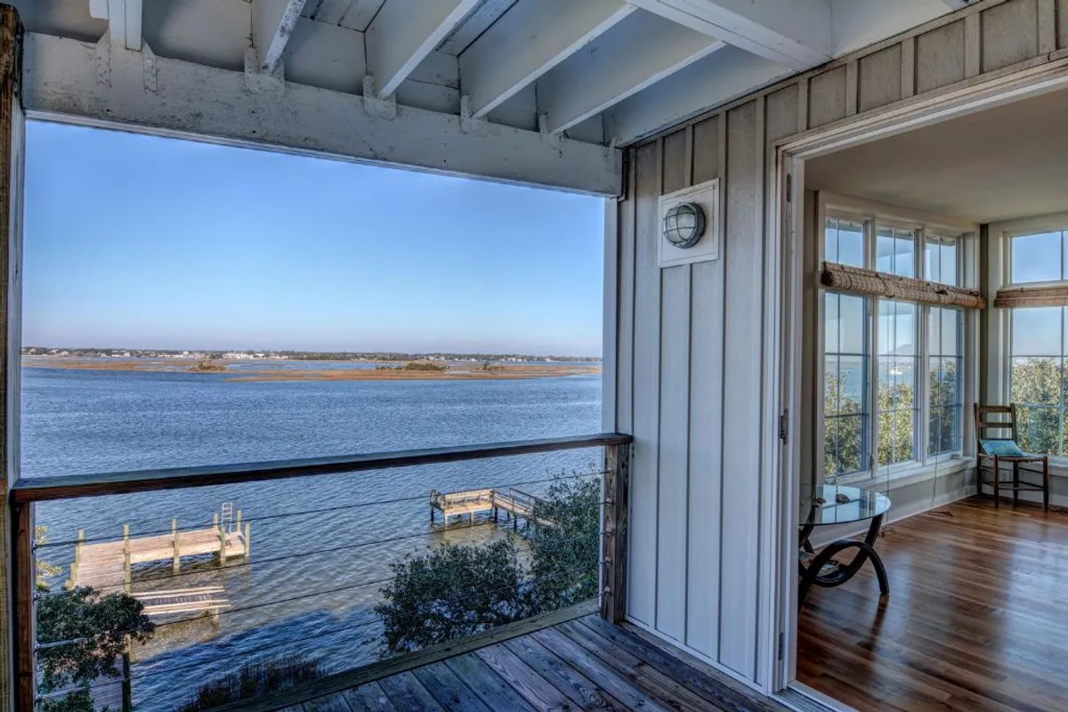A serene balcony scene with a view of tranquil water, a wooden deck, large windows, and comfortable furniture—perfect for relaxing, reading, or taking in the scenery.