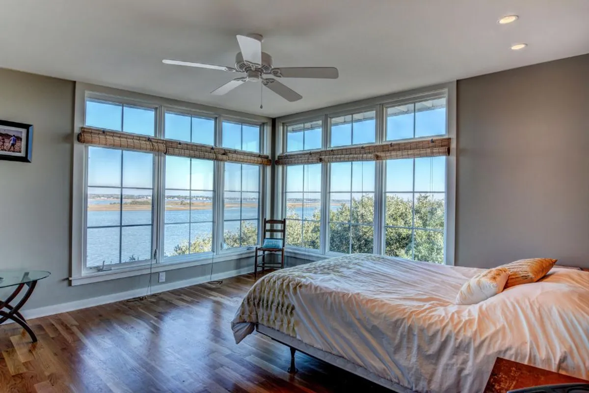 A peaceful bedroom featuring a comfortable bed positioned near large windows that offer scenic views and abundant natural light. The space is accented by warm wooden flooring, creating an inviting and restful atmosphere ideal for relaxation.