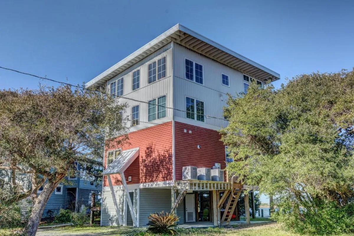 A modern home with a distinctive red and white exterior sits elevated above the surrounding greenery. An expansive deck offers ample space for outdoor gatherings, meals, and enjoying the fresh island air.