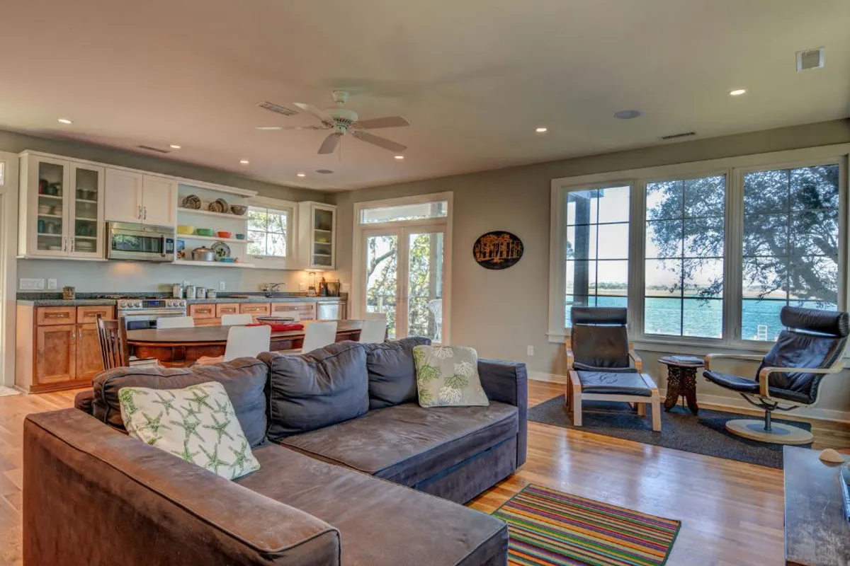 This image features a spacious, open-concept layout with a large sectional sofa, a kitchen area, dining table, and wide windows that offer scenic views. The interplay of comfortable seating, communal dining, and abundant natural light reflects the inviting spirit of the gathering spaces described in the section.