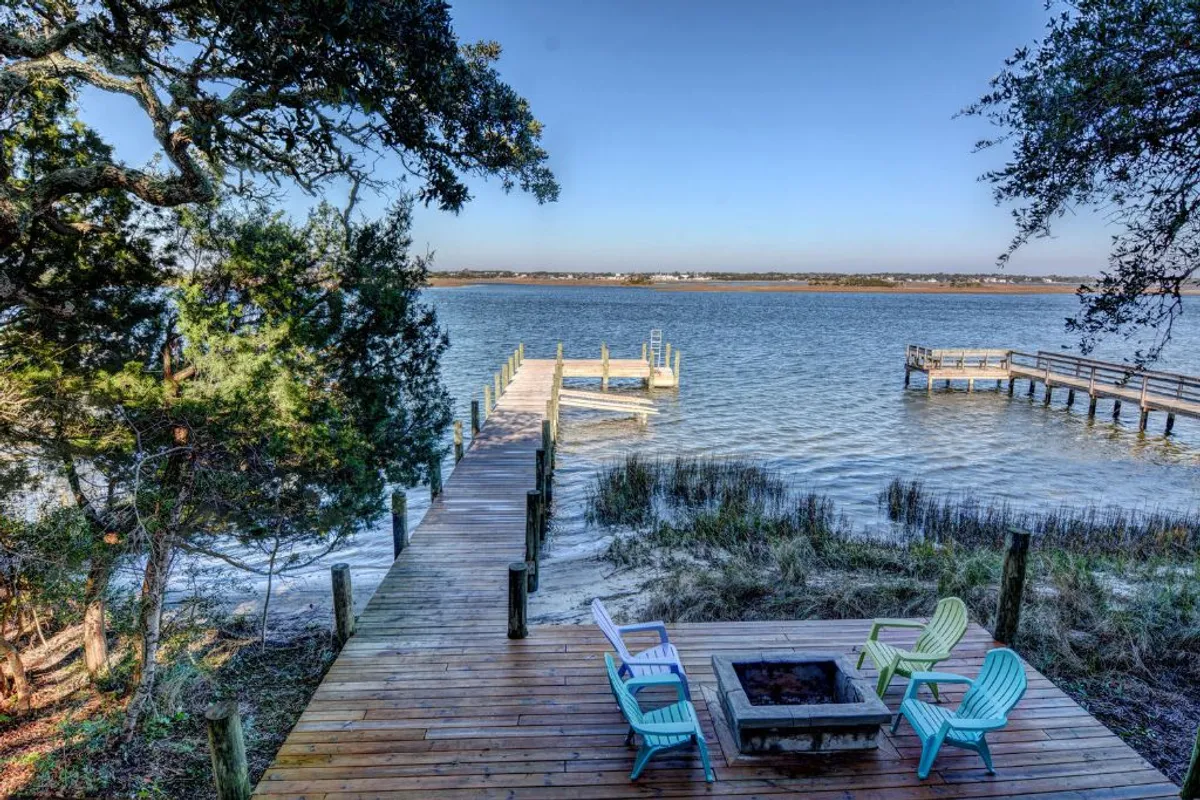 This exterior image captures a dock extending out onto the water, surrounded by lush trees, with a cozy fire pit in the foreground. The tranquil water setting invites moments of relaxation and peaceful reflection, while the dock hints at opportunities for outdoor activities such as fishing or boating.