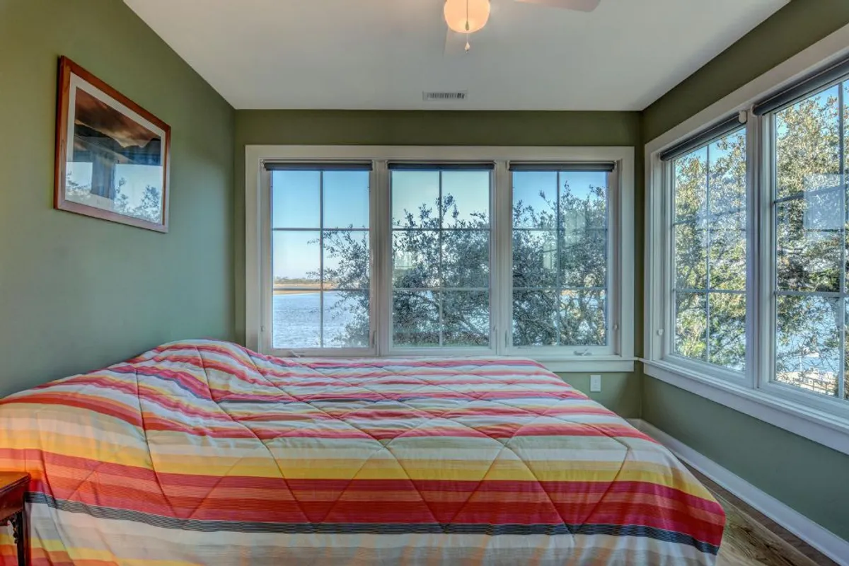 A bunk room with a comfortable bed topped with a colorful quilt, generous windows bringing in natural light and scenic views, and playful wall art. The setting is inviting for kids or younger guests, striking a balance of coziness and fun.