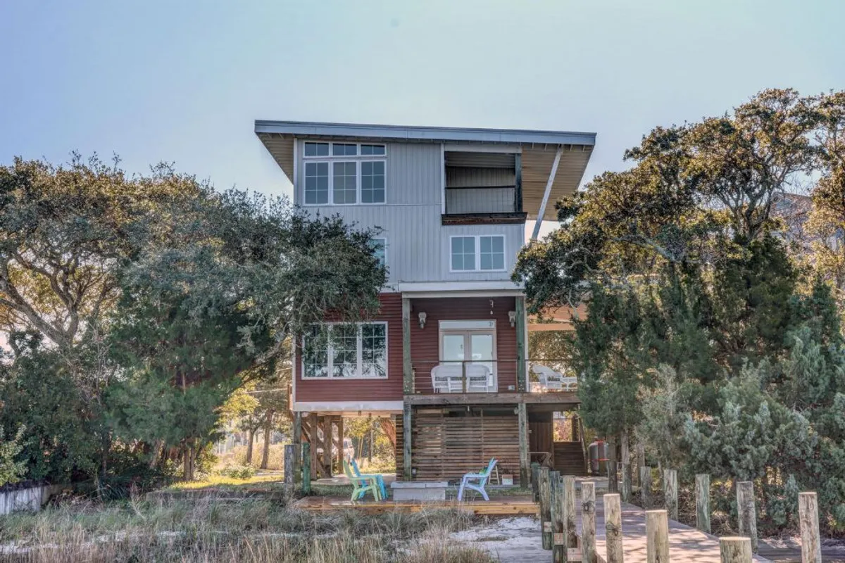 A striking example of modern architecture nestled in greenery features a welcoming outdoor seating area. The space is designed for comfort and relaxation, providing an ideal spot for gatherings or quiet moments in nature.