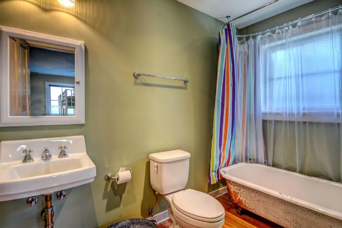 A bright bathroom characterized by a vintage bathtub with colorful shower curtain, complemented by a sink with reclaimed, vintage-style fixtures. The playful color and antique details embody both whimsy and nostalgia.