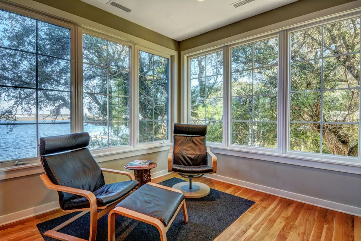 A serene interior scene featuring two black leather chairs and a round wooden table set by large windows, through which natural views and abundant daylight pour in. This bright workspace is inviting for reading, contemplation, or productive work, all while enjoying the beauty of the outdoors from within.